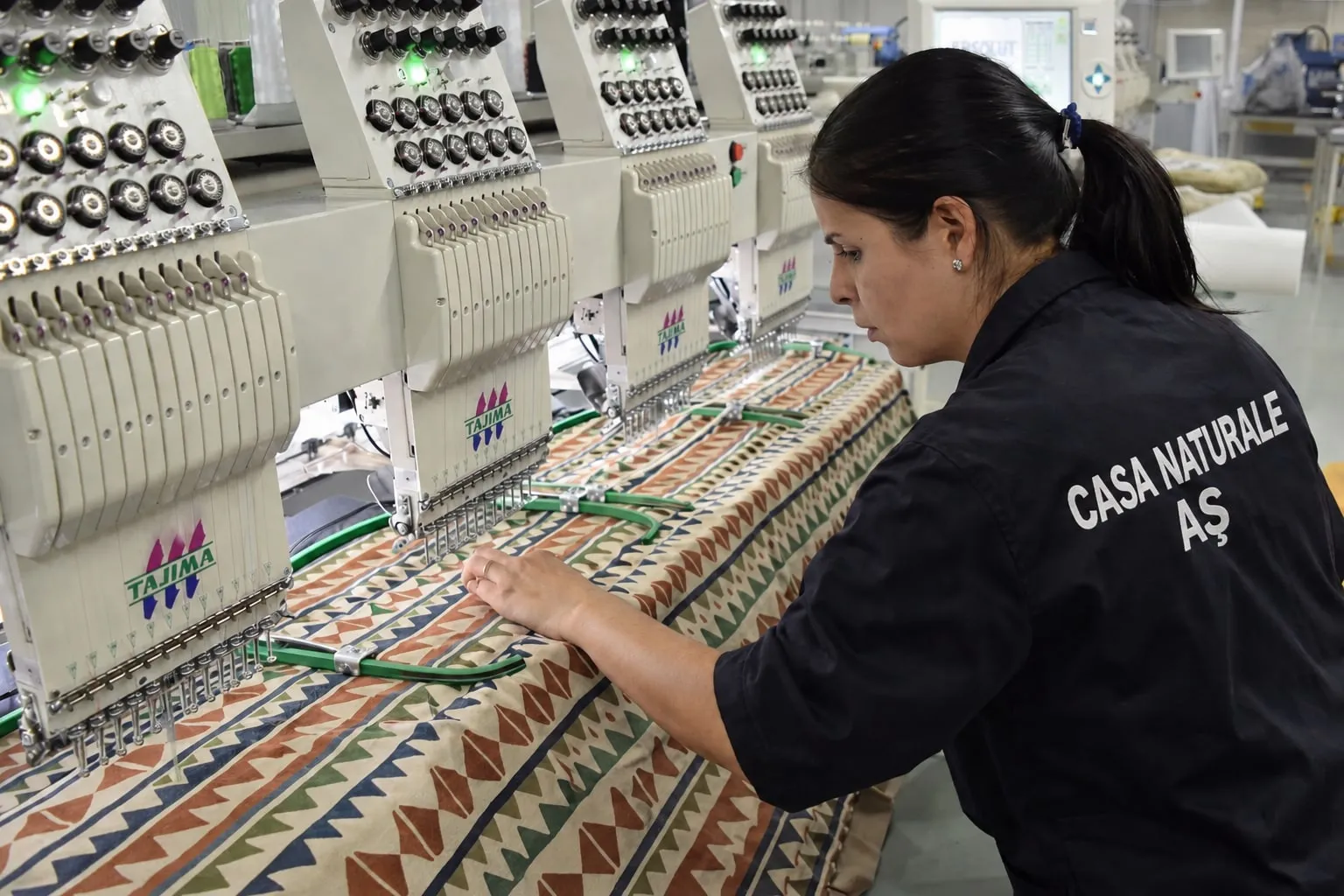 An operator at one of our Tajima embroidery machines, with a patterned fabric running through the frame.